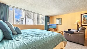 Ein Hotelzimmer mit einem großen Bett, einem Fernseher, einer Sitzecke und Blick auf hohe Gebäude.