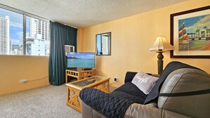 Ein Hotelzimmer mit großem Fenster, Fernseher, Sofa, kleinem Tisch und Lampe.