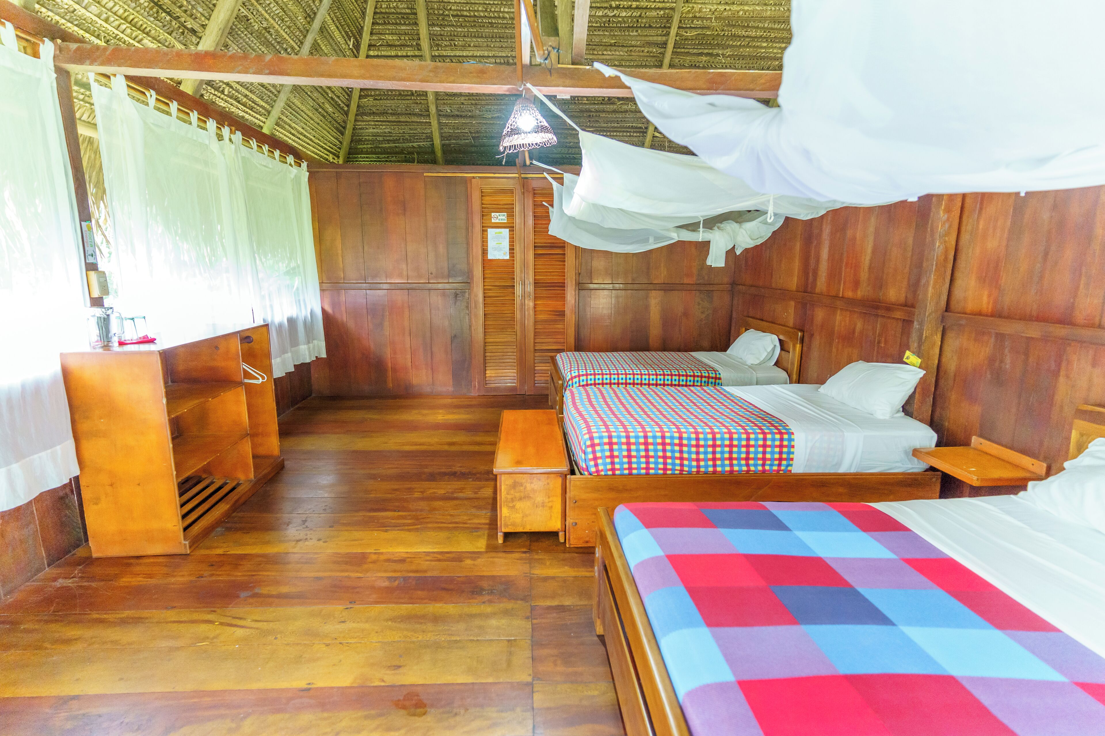 A room with two beds, wooden flooring, and a thatched roof.