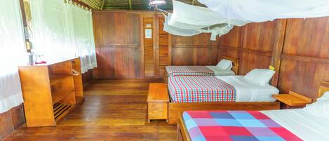 A room with two beds, wooden flooring, and a thatched roof.