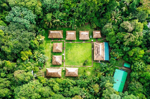 Vista aérea de un resort con cabañas de techo de paja dispuestas en forma de cuadrado, rodeado de exuberante vegetación tropical.