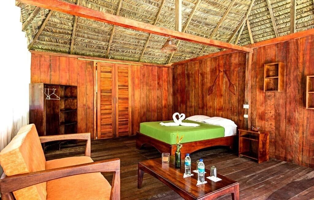 Una habitación de madera con una cama, una silla, una mesita y un armario.