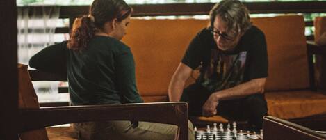 Two people playing chess in a room with a thatched roof and wooden furniture.