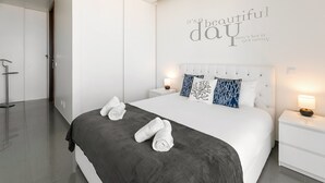 A modern bedroom with a large bed, white nightstands, and a wall with a motivational quote. - Nazaré Rooftop Oásis (Nazaré)