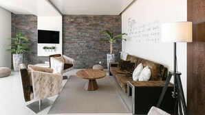 A modern living room with a stone wall, a flat-screen TV, a wooden coffee table, and a sofa with cushions. - Nazaré Rooftop Oásis (Nazaré)