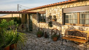 A stone building with a tiled roof, a bench, and potted plants. - Casas da Gralha - Alecrim (Alcobaça)
