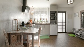 A modern kitchen with a wooden dining table and chairs, a built-in microwave, and a window with sheer curtains. - Casas da Gralha - Alecrim (Alcobaça)