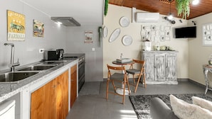 Een keuken met een granieten aanrecht, houten kastjes, een spoelbak en een kookplaat. Er zijn twee stoelen, een klein tafeltje en een kastje met decoratieve borden.