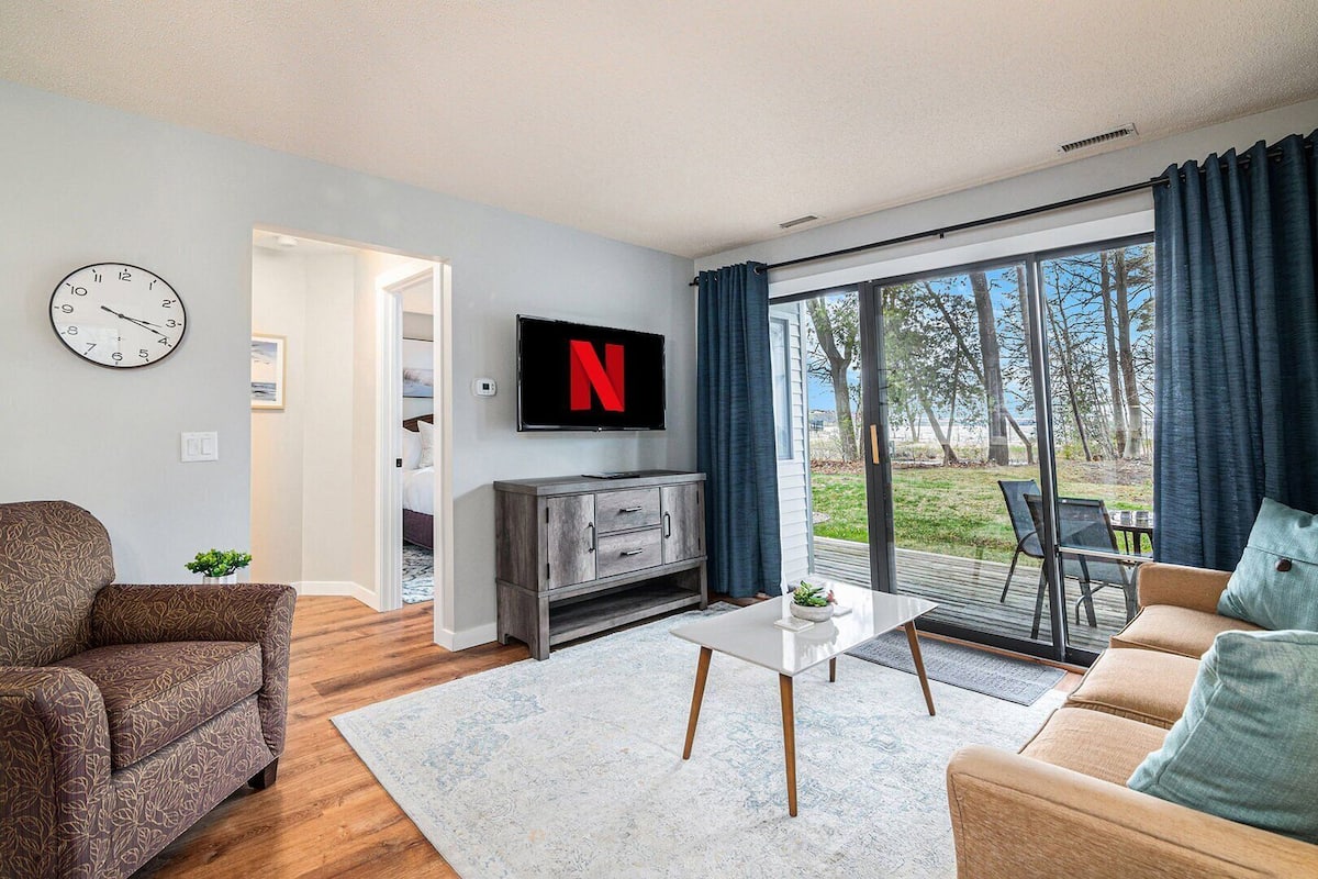 Una sala de estar moderna con un televisor grande, un reloj y vistas al exterior.