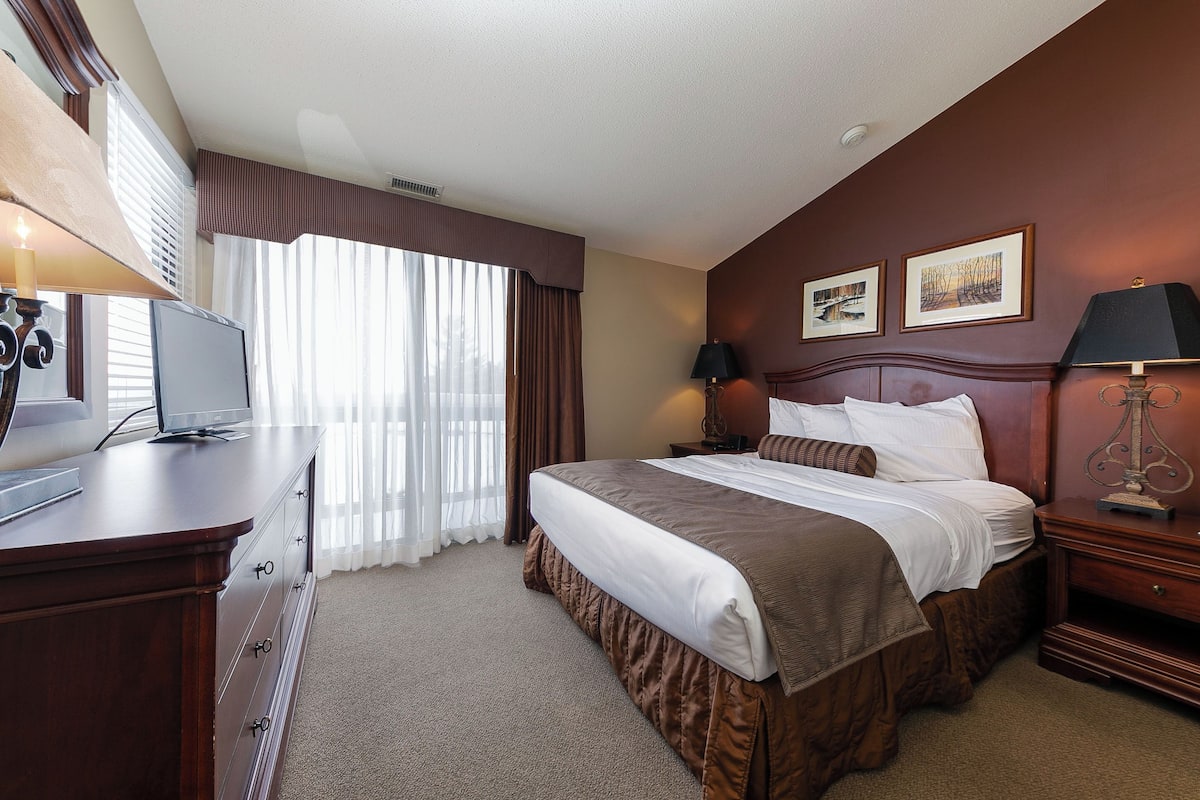 Habitación de hotel con una cama grande, un escritorio con computadora, una lámpara y dos cuadros en la pared.