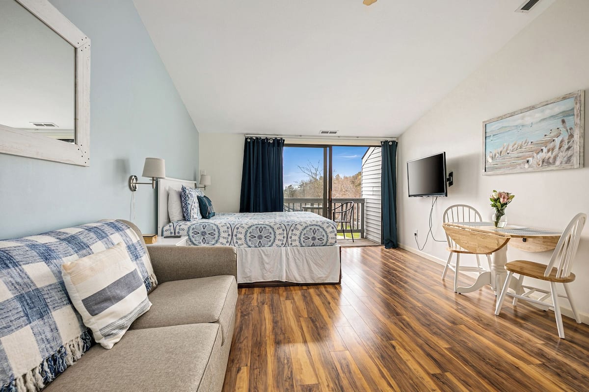 Un dormitorio con cama, sofá, mesa de comedor con sillas, televisor y ventana con cortinas.