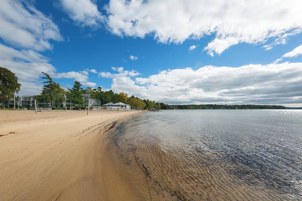 Una playa con orilla arenosa, aguas tranquilas y cielo despejado con nubes.