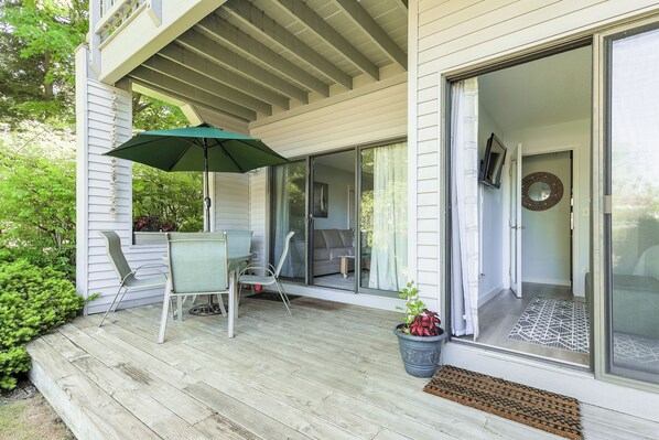 A covered porch with a table and chairs, a potted plant, and a sliding glass door leading to a room. - The Shores Resort (Williamsburg)