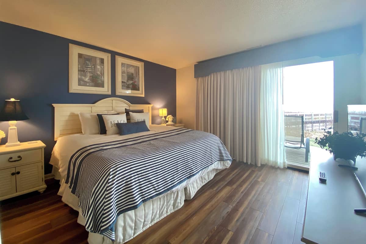 Un dormitorio con cama, mesitas de noche, una ventana con cortinas y vistas al exterior.