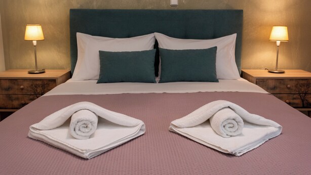 Cama bem arrumada com duas almofadas, uma cabeceira e duas luminárias laterais.