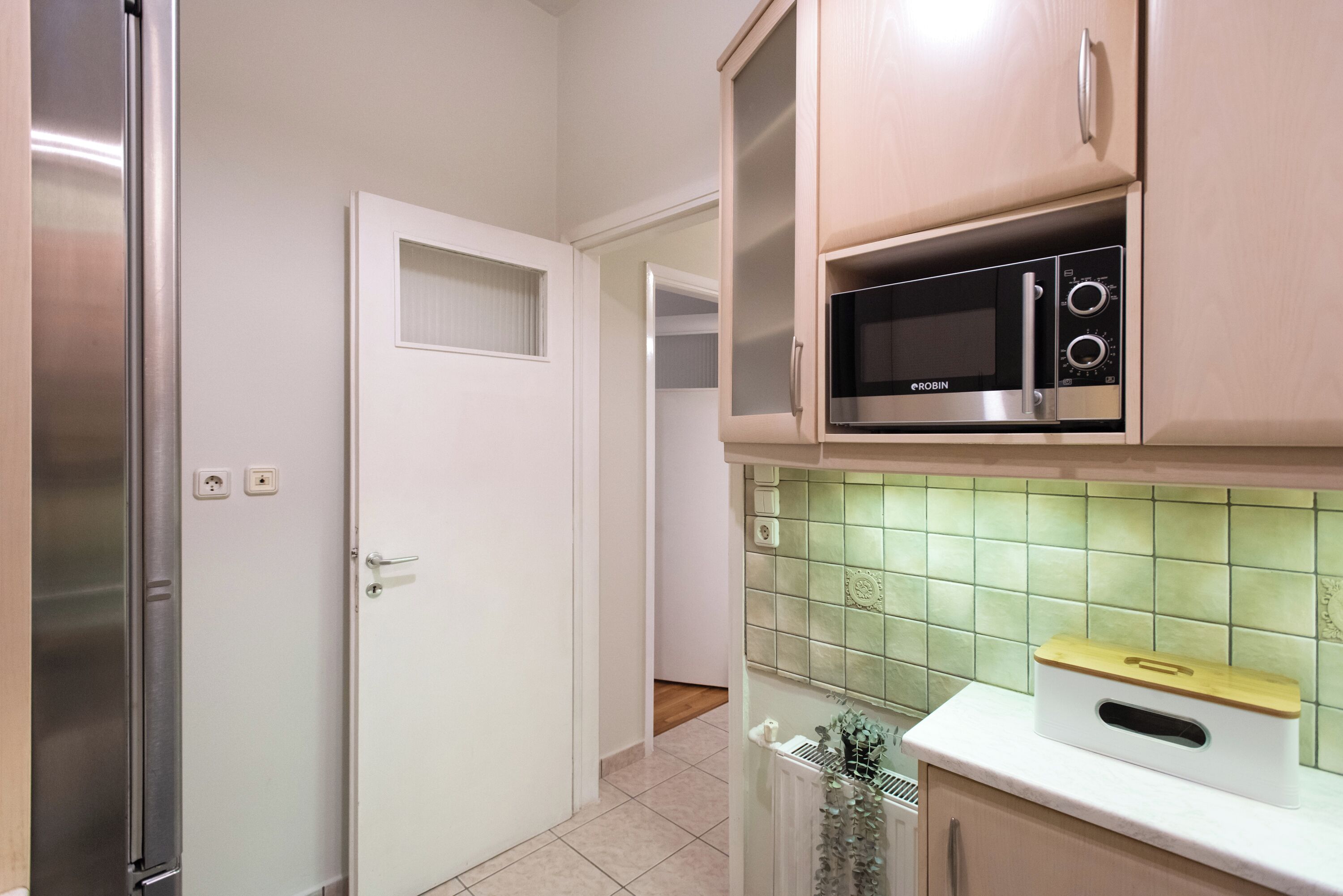 Una cucina compatta con forno a microonde integrato, frigorifero e schienale piastrellato.