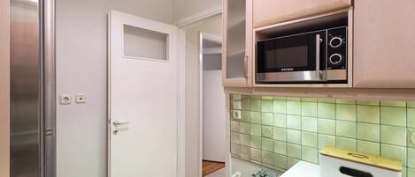 A compact kitchen with a built-in microwave, a refrigerator, and a tiled backsplash.