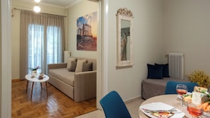 Quarto de hotel com sofá, mesa de jantar com prato e vinho, pintura de ruínas antigas e radiador.