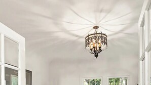 Amplia sala de estar con un sofá de cuero marrón, una mesa de centro de madera y una alfombra estampada. Un candelabro cuelga del techo y hay ventanas grandes con vista a la vegetación.
