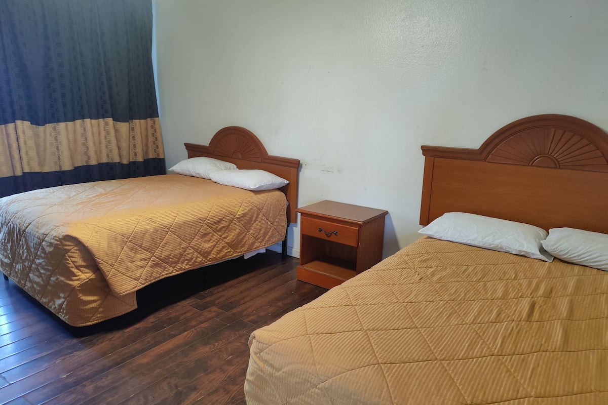 Two single beds with wooden headboards, a small wooden nightstand with a drawer, and a plain white wall.