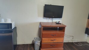 Ein kleines Zimmer mit einem Holzkasten, einem Papierkorb, einer Mikrowelle und einem an der Wand befestigten Fernseher.