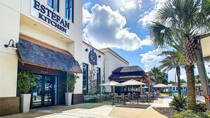 A hotel named 'ESTERAN KITCHEN' with a modern facade, outdoor seating area, and palm trees.