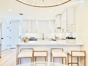 A modern kitchen with white cabinetry, a central island with bar stools, and a hanging light fixture.