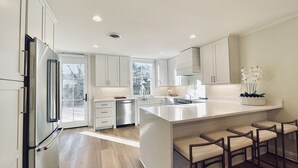 Een moderne keuken met witte kastjes, een roestvrijstalen koelkast, een inbouwoven en een groot kookeiland met barstoelen.