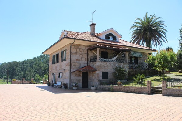 A two-story stone house with a balcony, a covered porch, and a large open patio area. - Paço AL (Monção)