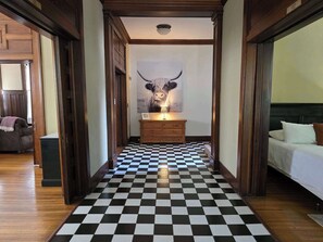 Un couloir d’hôtel avec un sol à carreaux, une commode en bois, un lit et un grand tableau représentant un taureau.