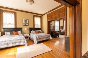 Une chambre avec deux lits, un plancher en bois, un grand miroir et une vue sur une autre pièce.