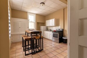 Une cuisine avec un sol carrelé, des placards blancs, une cuisinière et une fenêtre.