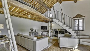 A spacious living room with a high ceiling, a staircase, and a fireplace.