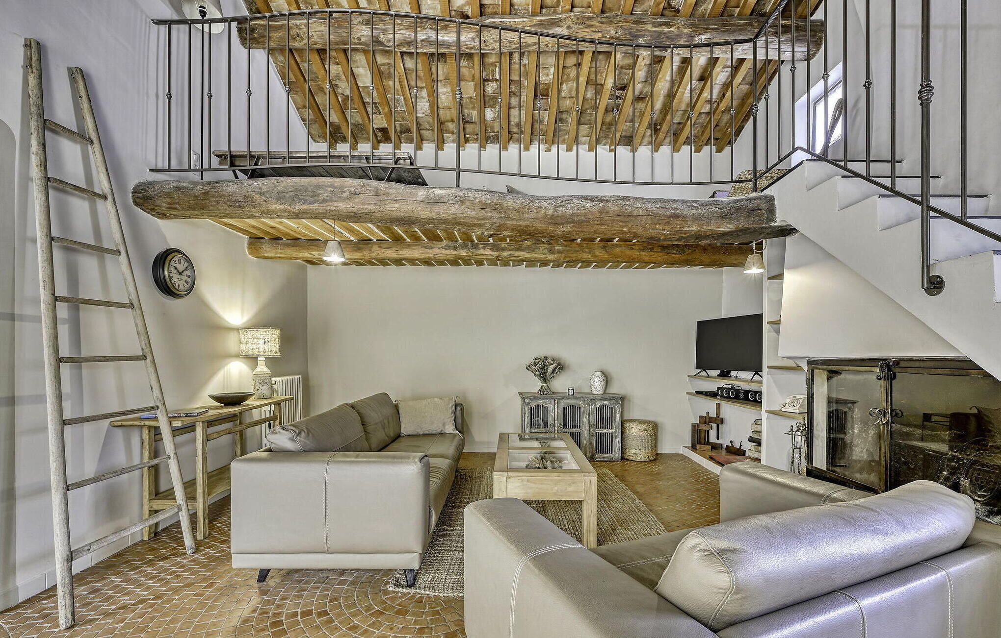 A loft-style living space with exposed wooden beams, a staircase, a sofa, a coffee table, and a television.