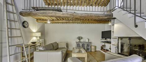 A loft-style living space with exposed wooden beams, a staircase, a sofa, a coffee table, and a television.