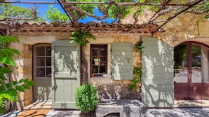 A rustic stone building with a tiled roof, a small window with shutters, and a door.