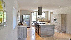 Une cuisine moderne dotée d’un îlot central, d’appareils électroménagers en acier inoxydable et offrant une vue sur l’extérieur.