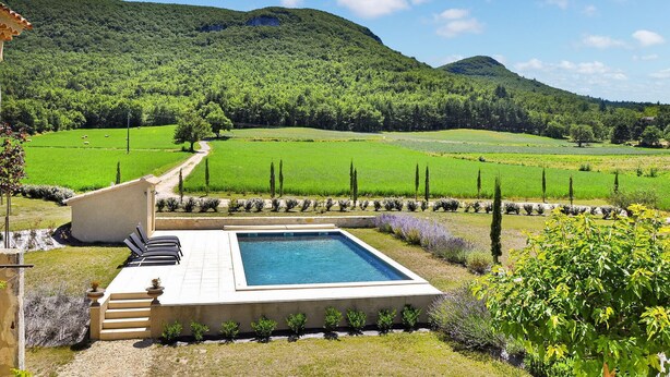 Un espace piscine offrant une vue sur un champ verdoyant et des montagnes.