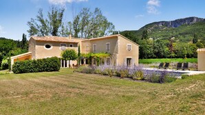 Une maison à deux étages, avec un toit recouvert de tuiles, entourée d’une pelouse bien entretenue et de plantes en fleurs.
