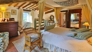 Un dormitorio con una cama grande, techo de madera, una silla de mimbre y un aparador.