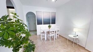 Ein Essbereich mit einem weißen Tisch und Stühlen, einer Kühlpflanze und einer Wandleuchte.
