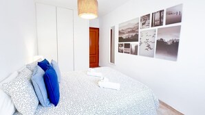 Ein Schlafzimmer mit einem Muster-Bettüberwurf, einer hängenden Leuchte und einer Wand mit gerahmten Fotografien.