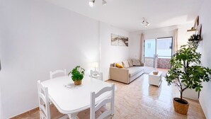 Ein modernes Wohnzimmer mit einem weißen Sofa, einem Esstisch mit Stühlen und einer Kühlpflanze.