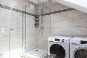 Un baño moderno con ducha de vidrio, lavadora integrada y pared de azulejos.