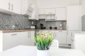 A modern kitchen with white cabinets, a tiled backsplash, and a white vase with flowers on the counter.