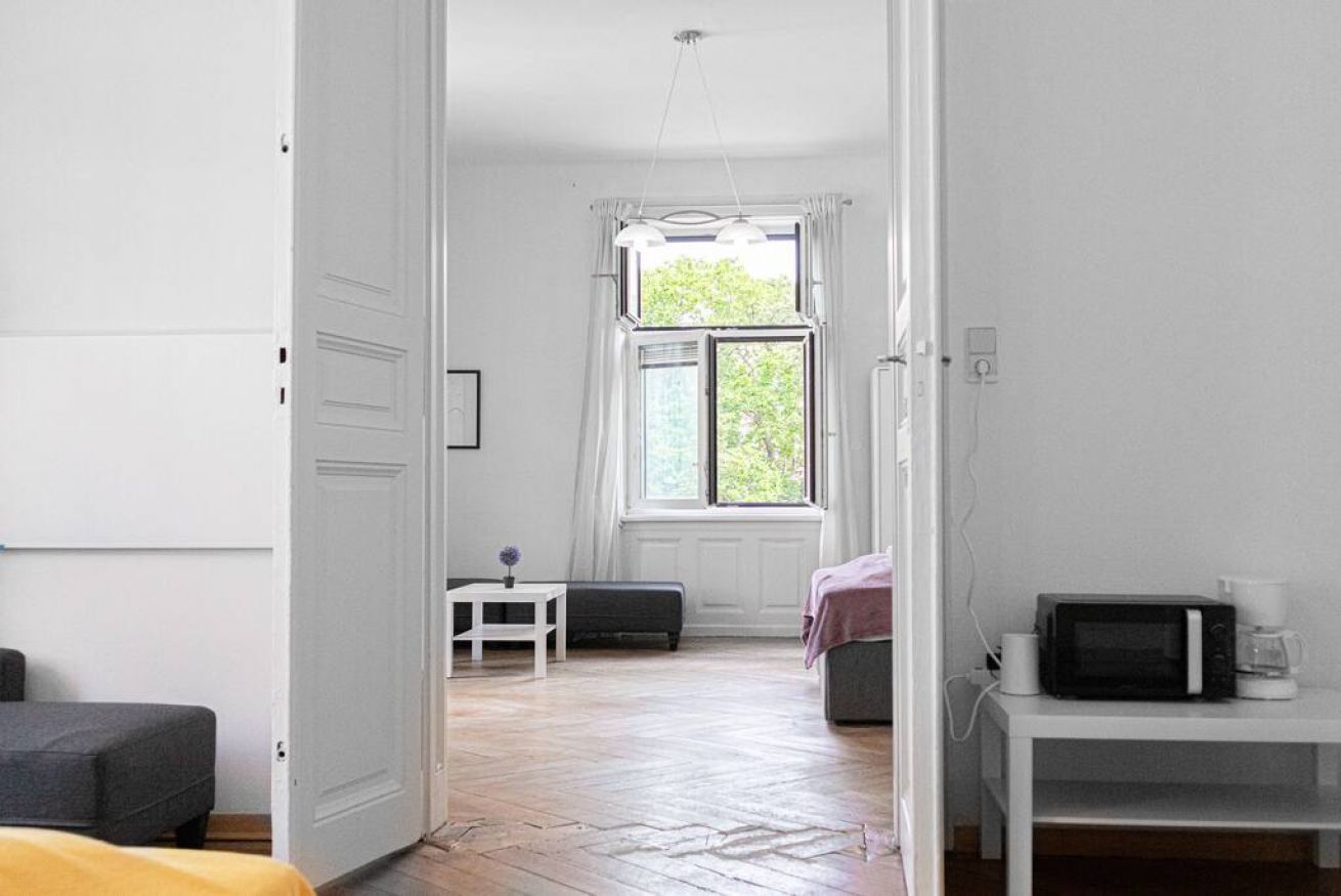 Ein Zimmer mit Bett, kleinem Tisch, Fenster mit Vorhängen, einer Mikrowelle und einer Kaffeemaschine.