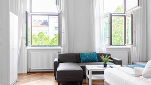 Un salon moderne avec un canapé gris, une table basse blanche et une vue sur la verdure à l’extérieur.