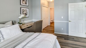 Un dormitorio con cama, mesita de noche, una silla y una puerta que da a un baño.