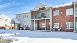 Un edificio residencial de dos pisos con balcón, fachada de ladrillo y suelo cubierto de nieve.
