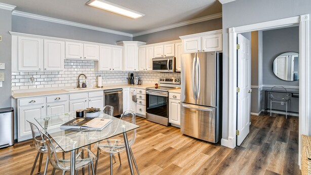Una cocina moderna con armarios blancos, electrodomésticos de acero inoxidable y una mesa de comedor de vidrio.